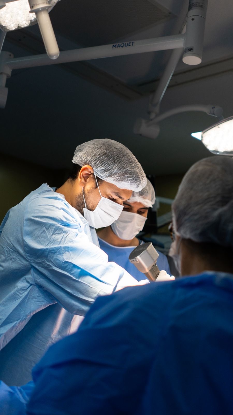 Dr. Luigi Freire, com máscara e avental, atuando com a equipe em centro cirúrgico